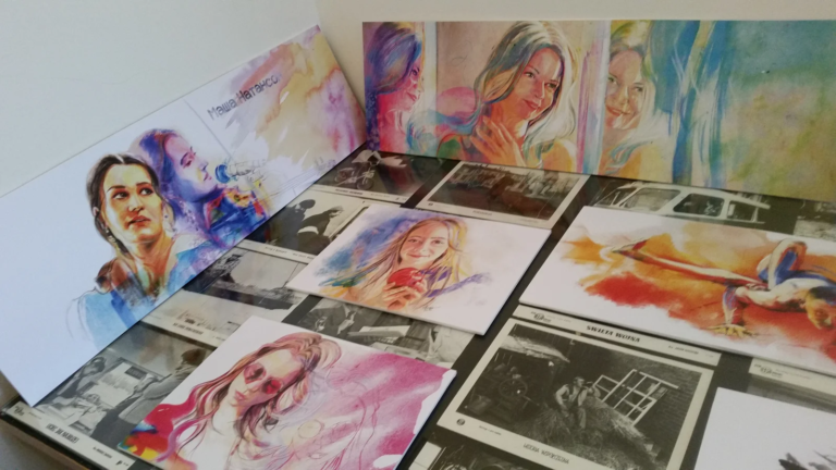 Kolorowe portrety rozłożone na stole przed zawieszeniem, wystawa ilustracji portretowej Zwierciadło duszy, Galeria Sztuki TAŚMA, Poznań 2016